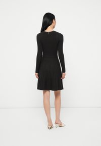 Abito in maglia nera a coste con maniche lunghe, corpetto aderente e gonna svasata. Presenta un colletto rotondo e un dettaglio di chiusura sul retro.
