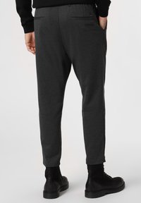 Tmavě šedé zúžené kalhoty vyrobené z texturované látky, s kapsami na zadní straně a navržené v uvolněném stylu, spárované s černými kotníkovými botami.