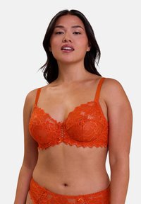 Reggiseno in pizzo di un vivace arancione, con bordi scallop, motivi floreali e un design frontale decorativo con spalline regolabili.