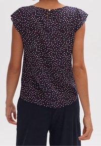 Blusa blu navy realizzata in un tessuto morbido e testurizzato, caratterizzata da un motivo a macchie multicolori e maniche corte con volant. Chiusura con bottoni sul retro.
