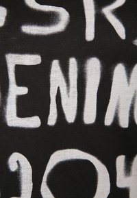Black fabric with large, white, spray-painted style letters forming the partial words "ENI" and other indistinct text.