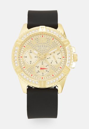 Goldfarbene Uhr mit rundem Zifferblatt, schwarzem Gummiband, Kristallakzenten, drei kleinen Zifferblättern und auffälligen Stundenmarkierungen in Rot und Schwarz.