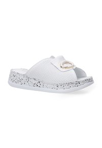 Witte geperforeerde slidesandalen met een brede band en een ronde gouden accent, met een gestructureerde spikkelige witte en zwarte zool.