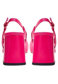 Klarröda högklackade sandaler med ankelsnören, klossklackar och svarta sulor, visade bakifrån mot en vit bakgrund.