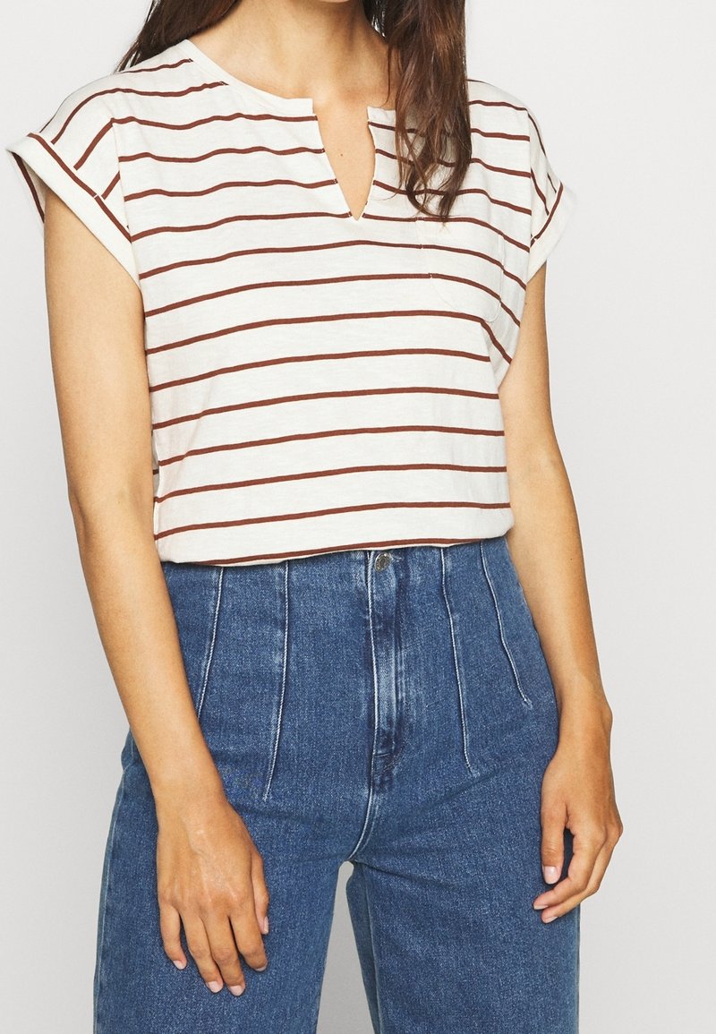 T-shirt à manches courtes rayé en crème avec des rayures horizontales bordeaux, doté d'un col en V et d'une coupe décontractée. Associé à un jean en denim bleu taille haute.