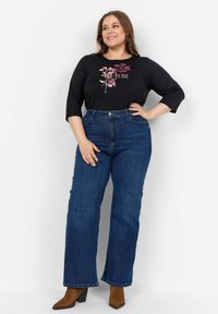 Melna blūze ar rozā ziedu dizainu un tekstu "COUTURE", kombinēta ar augsto vidukli zilām džinsu biksēm ar brīvu piegriezumu un smalko diegu šuvēm.