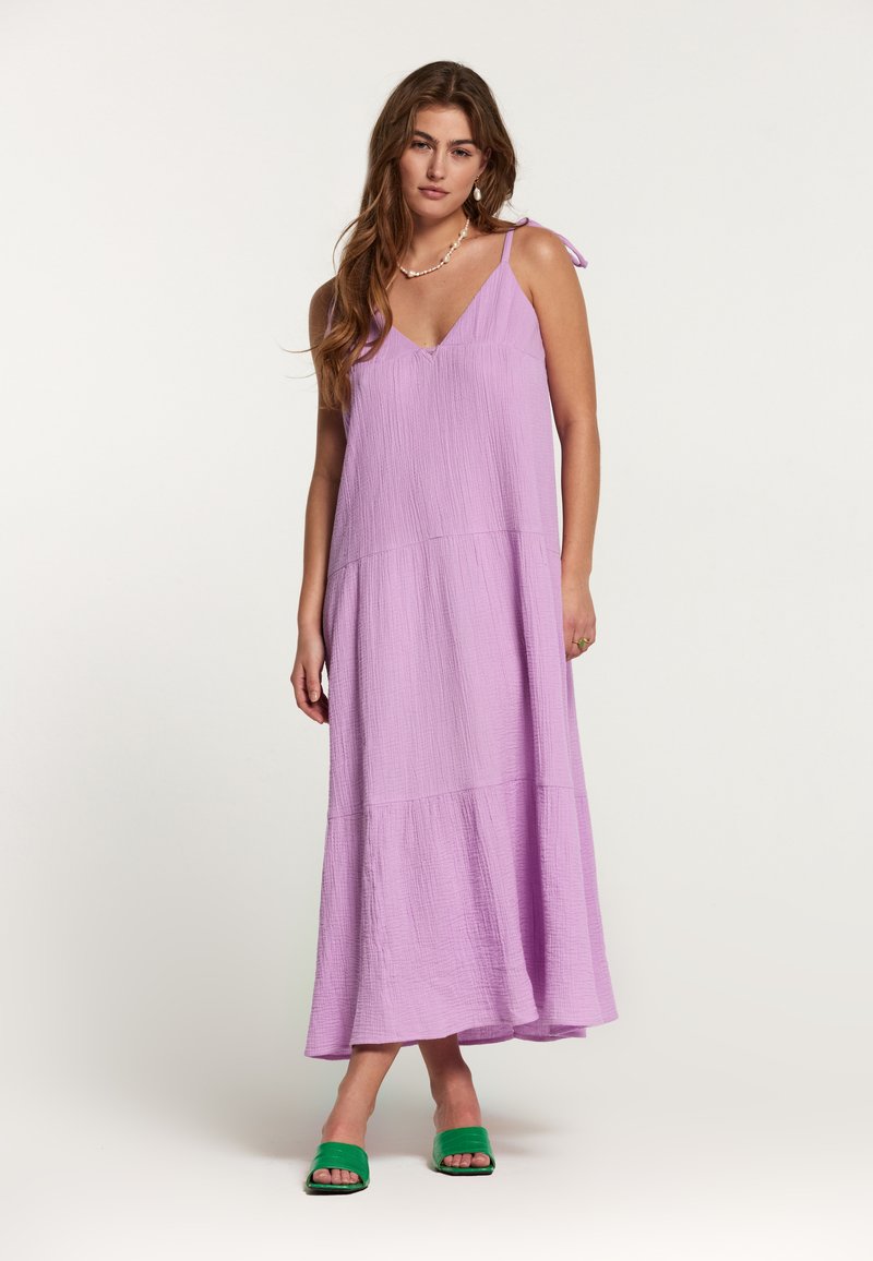 Rochie maxi de culoare lila, cu decolteu în V, dintr-un material texturat, și bretele subțiri. Prezintă un design în straturi. Pur și simplu purtată cu sandale verzi tip slide.