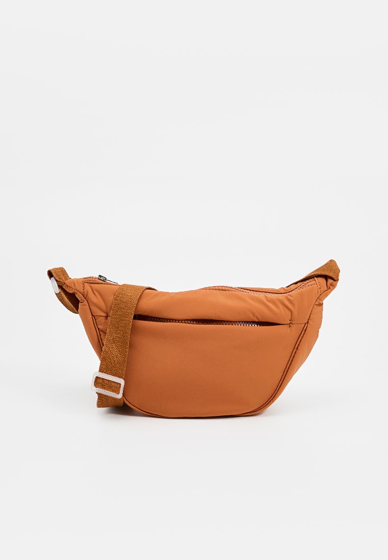 Sacoche marron rembourrée en synthétique avec une forme courbée, une bandoulière réglable et une poche frontale zippée. Texture lisse et accents minimaux.