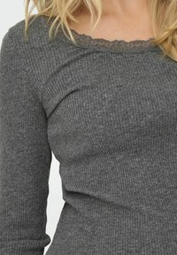 Sivi dugosleeve top s rebrastom teksturom i čipkastim ovratnikom. Tkanina izgleda mekano i rastezljivo, s oblikovanim dizajnom.