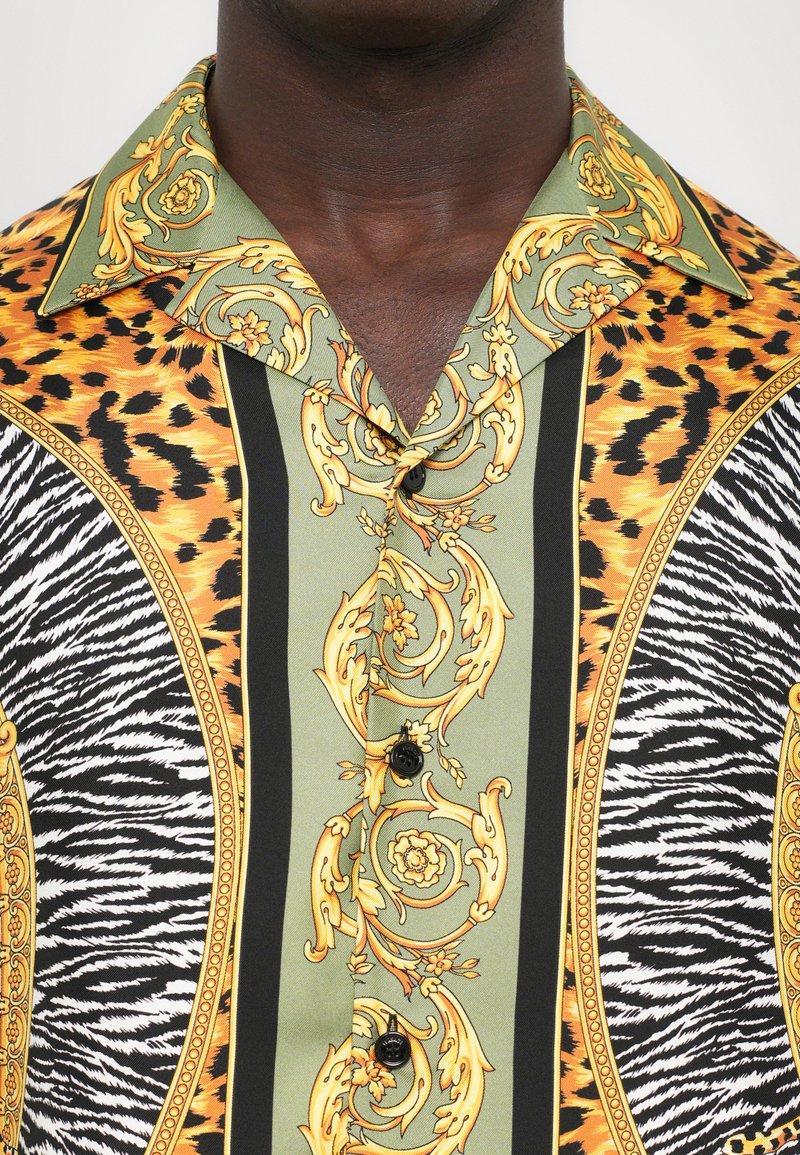 Korte mouw blouse met groene en gouden bloemenpatronen, oranje luipaardprint en zwart-witte zebra strepen, met zwarte knopen.