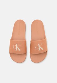 Sandales à glissière de couleur pêche avec une sangle en tissu douce arborant un logo blanc de Calvin Klein Jeans ; semelle en caoutchouc lisse, design à bout ouvert.