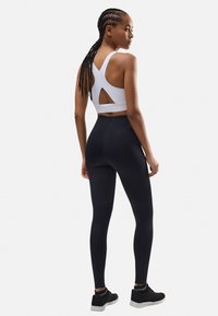 Sujetador deportivo blanco con espalda recortada, combinado con leggings negros de cintura alta y zapatillas deportivas negras. Tela suave, diseño ajustado.