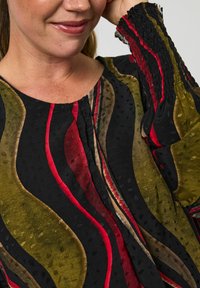 Multifarvet bluse i nuancer af sort, rød, oliven og guld; har bølgede mønstre og struktureret stof; elastiske manchetter tilføjer detaljer.