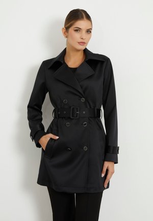 Manteau noir en tissu lisse, présentant un design croisé, un large col, une ceinture avec boucle et des poches latérales.