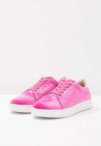 Baskets en velours rose avec semelles en caoutchouc blanches, dotées de lacets plats et d'œillets dorés. Texture lisse avec un bout arrondi et des détails de couture subtils.