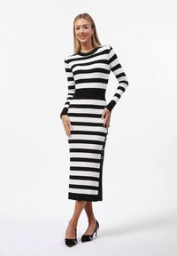 Schwarz-weiß gestreiftes, geripptes Strickkleid mit langen Ärmeln, schmaler Schnitt, knopfdetail an der Seite, knielang, rundhalsausschnitt.