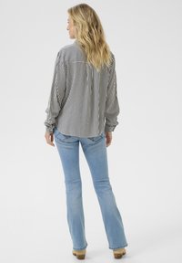 Camicia a righe bianca e nera con maniche lunghe, dettaglio sul retro e polsini con bottoni; abbinata a jeans svasati blu chiaro.