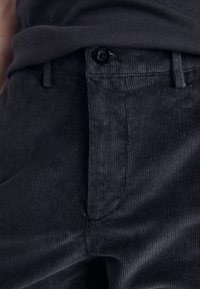 Pantalon en velours côtelé gris foncé avec des côtes verticales, doté d'un bouton noir et de poches latérales. Le tissu semble doux et texturé.