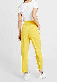 Geel op maat gemaakte broek met een hoge taille, een gladde tekstuur, twee achterzakken en een rechte pijp, gecombineerd met een witte aansluitende top en witte sneakers.