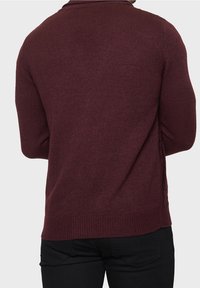 Vínově červený pletený svetr s texturovaným povrchem, s kulatým výstřihem a bočním copánkovým detailem. Upnutý střih, žebrované manžety a lem.