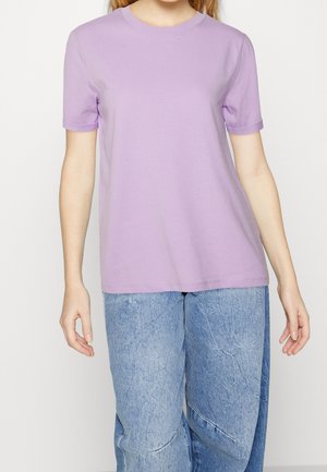 Koszulka z krótkim rękawem i okrągłym dekoltem, wykonana z jasnofioletowej bawełny. Charakteryzuje się luźnym krojem i gładką fakturą. Połączona z jasnoniebieskimi, wysokim stanem jeansami.