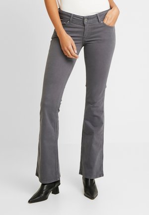 Jeans grises de campana con una textura suave, bolsillos frontales, presillas para cinturón y cierre de cremallera. Llevados con botas de tacón negro hasta el tobillo.