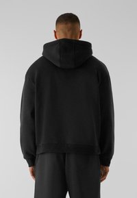 Sweat à capuche noir au coupe décontractée, avec des bords côtes aux poignets et à l'ourlet, et une texture douce. Les détails de couture au dos ajoutent un intérêt design subtil.