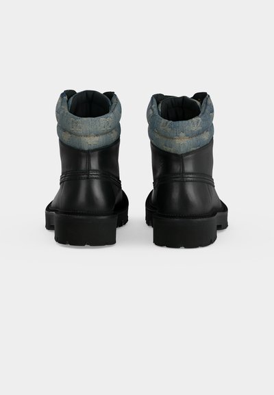 Paire de bottines en cuir noir avec semelles épaisses et poignets en tissu bleu rembourrés avec un motif subtil, vues de dos.
