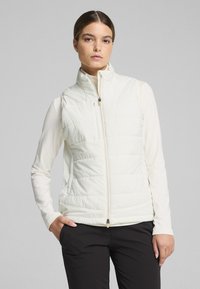White padded vest with a high collar, front zipper, and side pockets, worn over a long-sleeve top. Smooth texture with a quilted design.