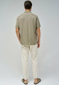 Camisa de botones de manga corta en color caqui, pantalones claros de color crema y zapatos marrones sin cordones con puntera redondeada y textura suave.