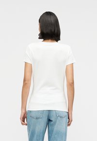 Λευκό κοντομάνικο μπλουζάκι από βαμβάκι, με στρογγυλή λαιμόκοψη. Φορεμένο με ανοιχτόχρωμο μπλε τζιν, που παρουσιάζει χαλαρή σιλουέτα.