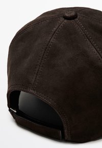 Cappello in suede marrone con costruzione a sei pannelli, cuciture visibili e una cinturino regolabile sul retro. Texture liscia e forma arrotondata.
