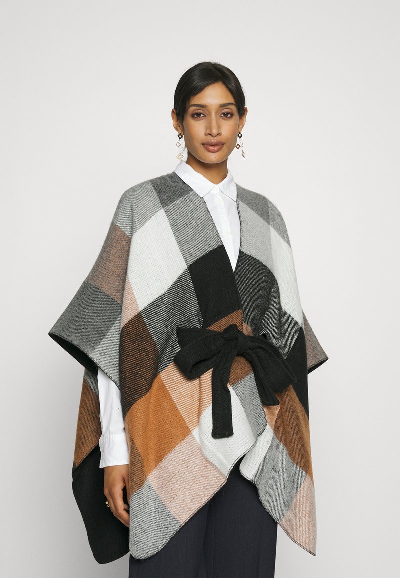 Poncho de punto en cuadros negro, gris, blanco y marrón, con un cinturón de tela negra. Presenta un diseño holgado y una textura suave.