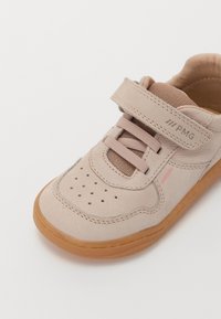Beige syntetiske sko med gummisåle, borrelåsrem, nettingdetaljer og perforert tå for pusteevne. Inneholder en liten rosa detalj.