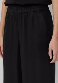Schwarze, leichte Hose mit einem elastischen Bund und Seitentaschen; glatte Textur und lockere Passform, geeignet für die Freizeit.