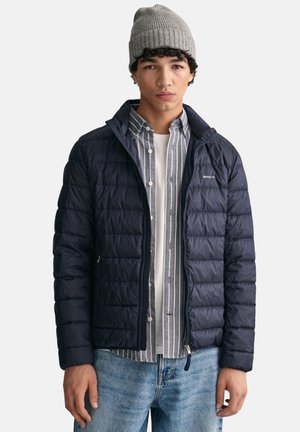 Navy puffer jacket with quilted texture, zippered front, worn over a gray and white striped shirt, paired with light blue jeans.