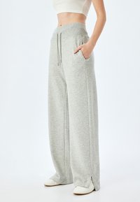 Lichtgrijze wijde sweatpants met een ribbelband, trekkoord, zijzakken en splitten aan de onderkant. Gemaakt van zachte, gestructureerde stof.