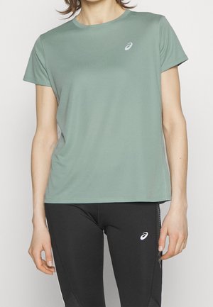 Osoba w jasnorozowej sportowej koszulce z krótkim rękawem i czarnych legginsach, oba z białym logo Asics.