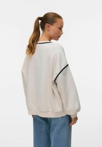 Lys grå oversize genser med sorte detaljer og ribbestrikkede ermer. Mykt stoff med en avslappet silhuett. Kombinert med løse jeans.