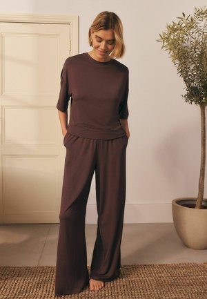 Braunes Loungewear-Set bestehend aus einem kurzärmeligen Oberteil und weit geschnittenen Hosen. Weicher Stoff, lässige Passform und Seitentaschen. Schlichtes, minimalistisches Design.