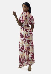 Maxi abito in tessuto leggero con un motivo floreale in rosso e beige. Vita elastica, maniche a palloncino corte e design fluido.