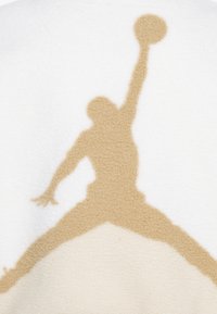 Tissu en polaire blanc avec une silhouette beige clair d'une figure sautant et tenant un ballon de basket. Texture douce et finition lisse.