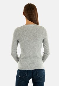 Maglione grigio a coste con maniche lunghe, scollatura rotonda, design aderente e texture liscia, indossato con jeans blu scuro.