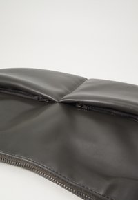 Sac en cuir noir avec une texture rembourrée, présentant une fermeture éclair le long du bord inférieur et une doublure intérieure lisse.