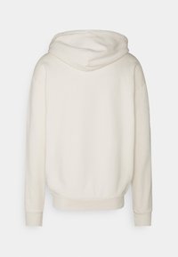 Krämfärgad hoodie i mjukt tyg med avslappnad passform, som har en känguruficka och ribbade ärmavslut. Avslutad med en dragsko i huvan.