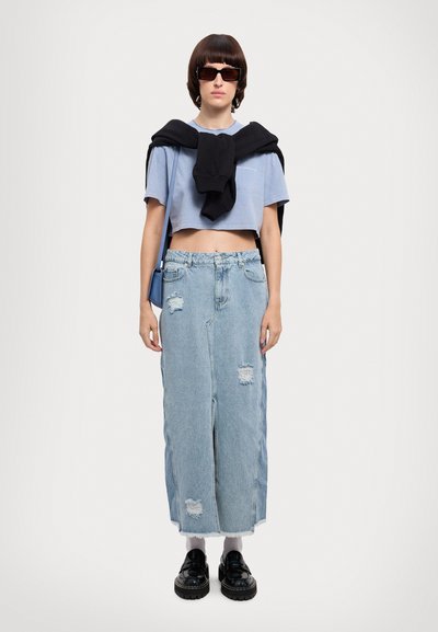 Light blue cropped t-shirt, black sweatshirt draped over shoulders, high-waisted distressed denim skirt, black platform shoes, rectangular sunglasses.