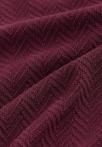 Strukturierter Stoff in tiefem Burgunderrot mit einem Chevron-Muster, das eine plüschige Oberfläche mit einer weichen, taktilen Qualität zeigt.