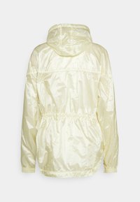 Ljust gult huva-jacka med en glänsande, slät yta. Har elastiska ärmslut och snörning i midjan. Enkel, odekorerad design.