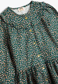 Vestido floral verde oscuro con flores rosas y amarillas. Presenta un cuello volado y botones dorados en la parte delantera. Tejido suave, falda con frunces.