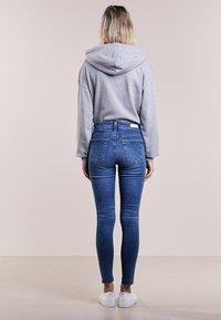 Šedá mikina s kapucí v kombinaci s modrými džíny s vysokým pasem. Džínovina má mírně vybledlý vzhled a hladký povrch. Bílé tenisky dotvářejí celkový vzhled.